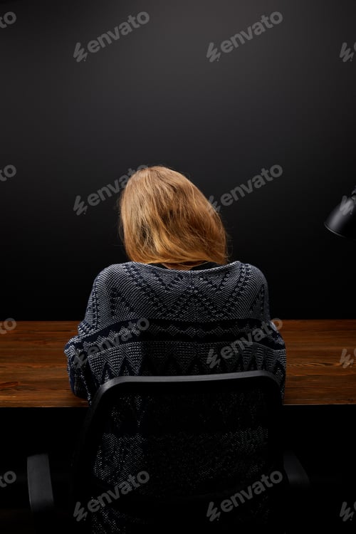 Preview: back view of woman sitting at wooden tabletop with black wall backdrop