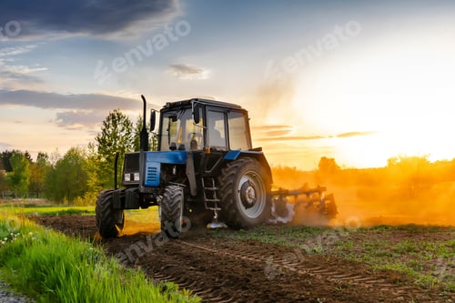 Preview: Modern blue tractor machinery plowing agricultural field meadow at farm at spring during sunset