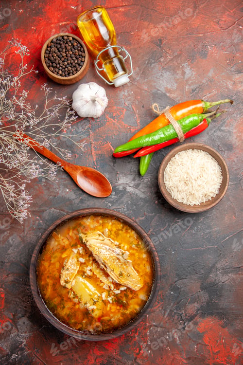 Preview: top view bowl of chicken soup wood spoon hot peppers bottle of oil bowl of black pepper rice on dark