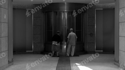 Preview: Grayscale shot of a couple of elderly by the glass doors of Gabriere station