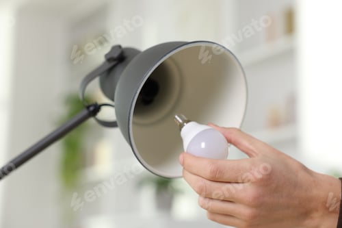 Preview: Man changing light bulb in lamp at home, closeup