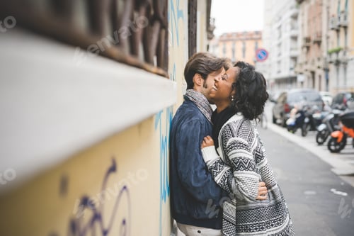 Preview: young handsome mixed race couple leaning against a wall, hugging and laughing