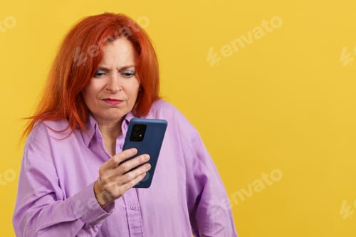 Preview: Worried redheaded mature woman using a mobile phone