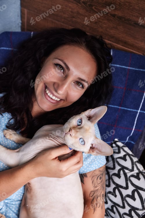 Preview: Playing with cat at home. Young woman sitting on couch and hugging pet.