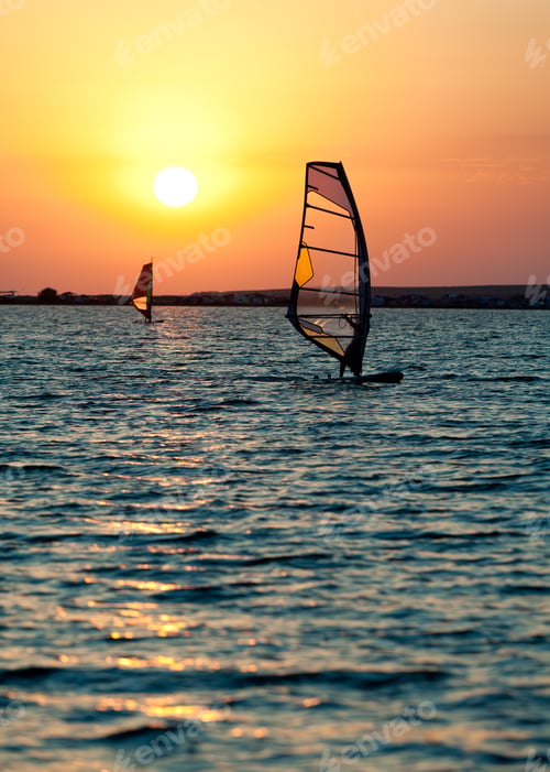 Preview: Still sea surface, man practicing wind surfing and golden sunset in sky