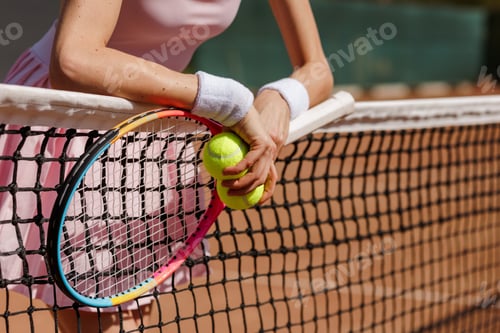 Preview: Female Tennis Player Holding Racket and Balls Resting on Net