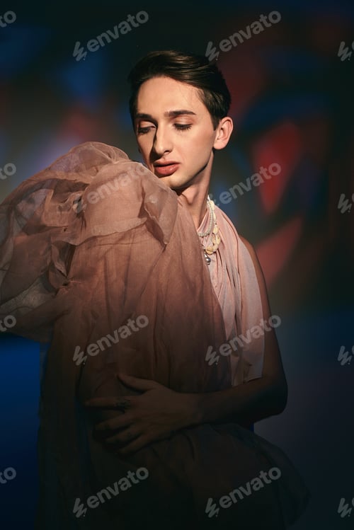 Preview: chic modish androgynous man in pastel elegant clothes looking away while on vibrant backdrop