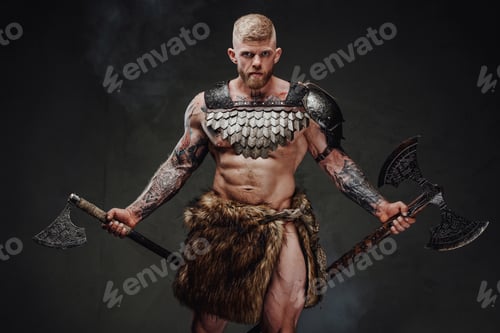 Preview: Brutal tattooed warrior wearing light armour and fur holding axes in dark studio