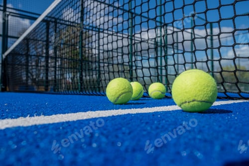 Preview: selective focus, four paddle tennis balls on a blue paddle tennis court close to the net