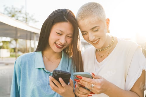 Preview: Happy teenage couple of friends with the cellphone and laughing in the modern city street