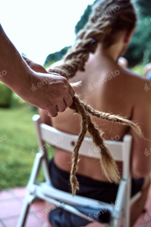 Preview: Close-up of a girl's hands, braiding a boy's dreadlocks in the garden.