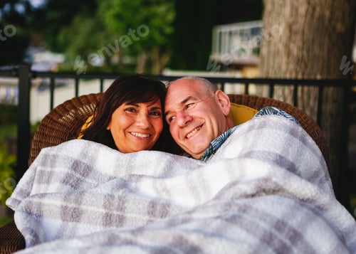 Preview: Latina, Hispanic woman happily snuggling under a plaid blanket with her smiling middle aged husband