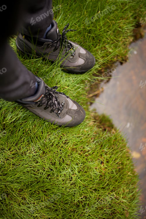 Preview: top view of hiker in boots standing on grass by water