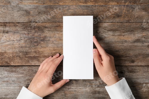 Preview: Woman holding blank brochure mock up on wooden table, top view