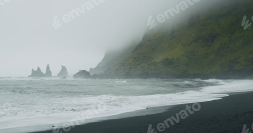 Preview: The black sand beach of Reynisfjara with waves hitting the shore on foggy rainy stormy day Vik