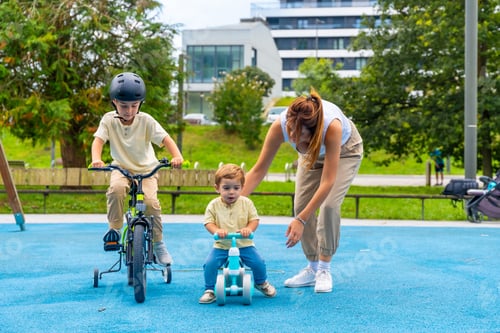 Preview: Mother helping children riding bikes in playground