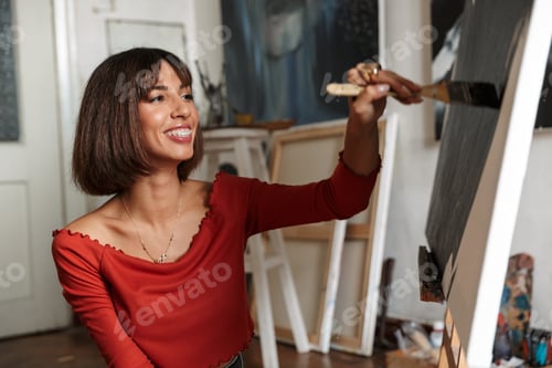 Preview: Portrait of young woman using painting tools while drawing in studio
