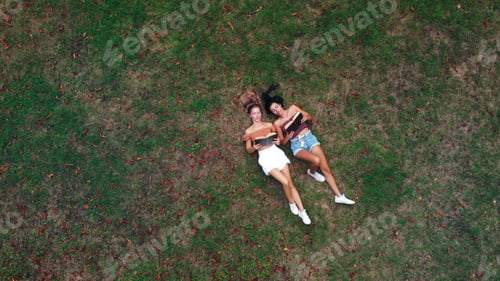Preview: Aerial top view of a female couple lying on the grass and reading books
