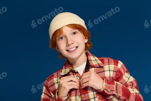 Preview: Redhead boy poses in casual clothes against a vibrant blue backdrop at the studio