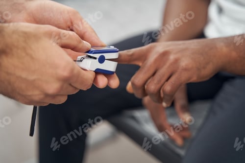Preview: Experienced physician attaching clip of pulse oximeter to male finger