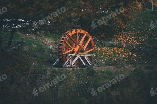 Preview: Old water wheel on the green grass with autumn trees in the background