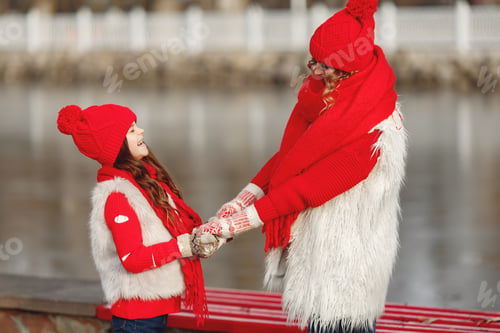 Preview: Mother and child in knitted winter hats play in winter park