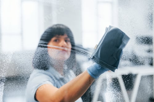 Preview: Woman cleaning dirty window by using towel. View through the glass
