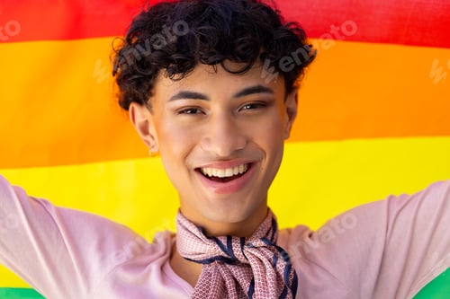 Preview: Smiling young man holding rainbow flag, celebrating transgender pride and identity