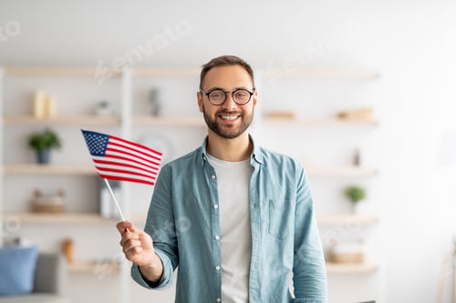 Preview: Handsome young guy holding American flag and smiling at camera indoors. Abroad education and student