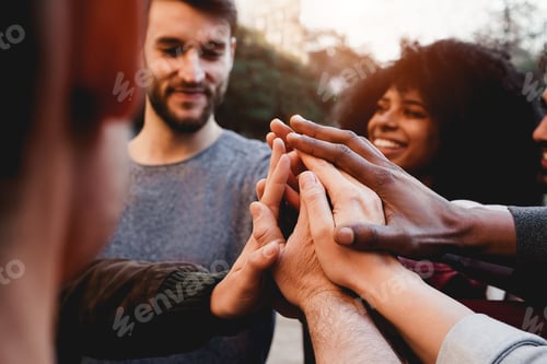 Preview: Multiracial young people celebrating together while stacking hands outdoor - Focus on hands