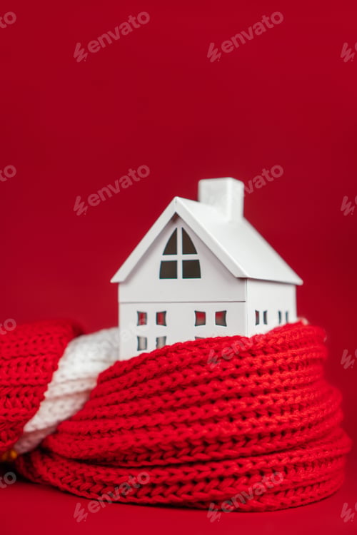 Preview: White toy house wrapped in red scarf on red background. Heating or insulating buildings concept