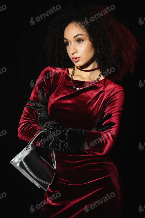 Preview: Stylish african american woman in dress posing with handbag isolated on black