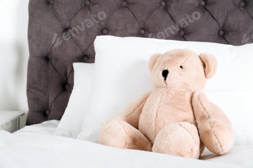 Preview: Cute teddy bear sitting on bed indoors. Space for text