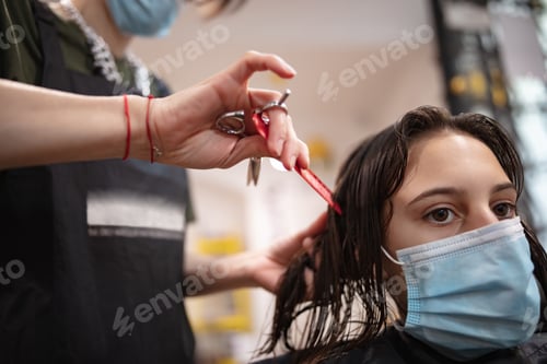 Preview: Hairdresser And Girl Child Customer In A Salon With Medical Masks During Virus Pandemic. Working