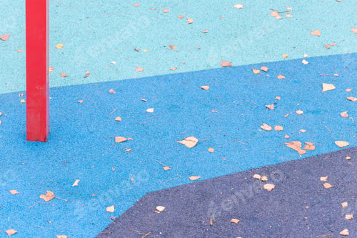 Preview: Blue rubber playground with red bars and fallen leaves: Active outdoor fun among triangular shapes.