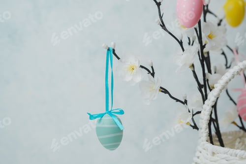 Preview: Festive blue striped Easter egg decoration with ribbon hanging on a flowering branch near basket