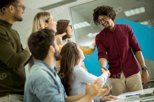 Preview: Group of young coworkers interacting around a table and handshaking in the office