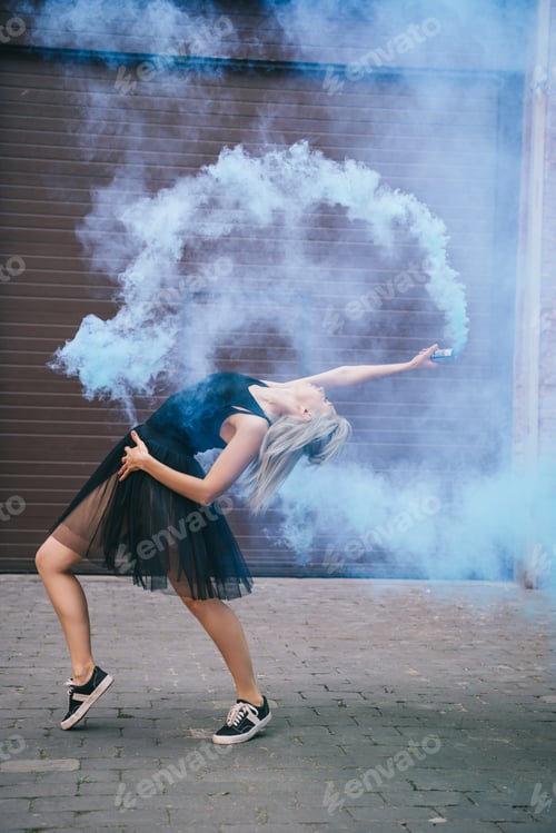 Preview: side view of young female dancer dancing in blue smoke on street