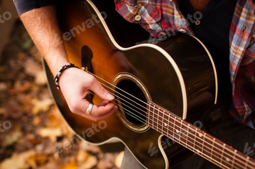 Preview: Cropped shot of young man playing guitar in autumn forest
