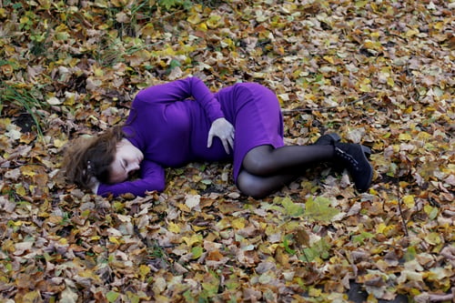 Preview: Pregnant woman lying in fetal position on autumn leaves loneliness, fear for the future of the child