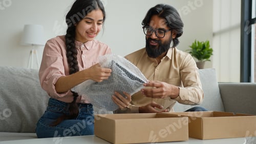 Preview: Happy couple customers receive parcel look inside box Arabian Indian man and woman open delivery