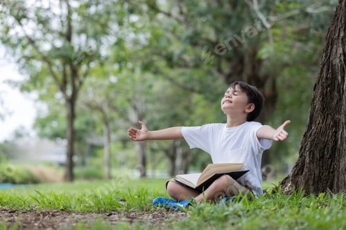 Preview: A joyful child sits under a tree with an open book, arms outstretched
