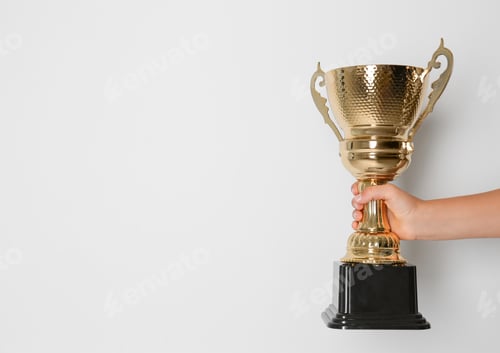 Preview: Child holding golden winning cup on light background, closeup. Space for text