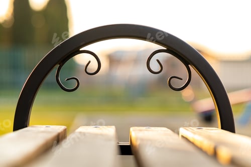 Preview: Closeup of wooden park bench with metal handgrip outdoors.