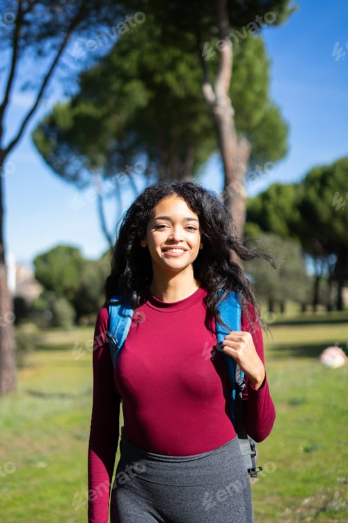 Preview: Young latin tourist walking in a park with backpack on sunny day