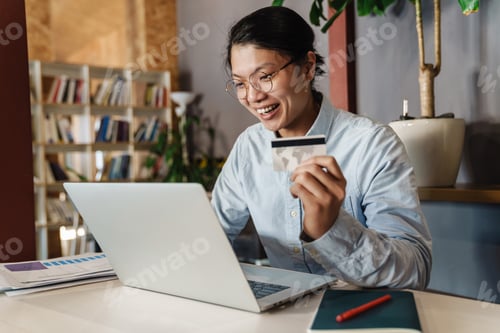Preview: Image of joyful handsome asian man using laptop and holding credit card
