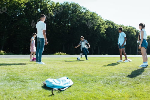 Preview: multiethnic teenage classmates playing with soccer ball in park