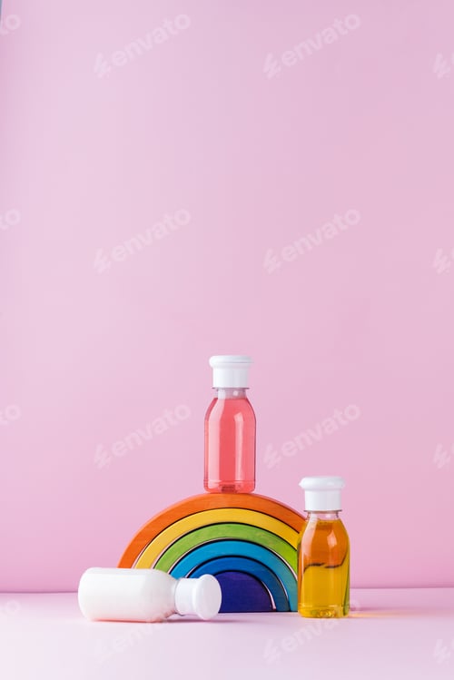 Preview: Baby detergents on a toy rainbow on a pink background. The concept of baby skin care. Copy space.