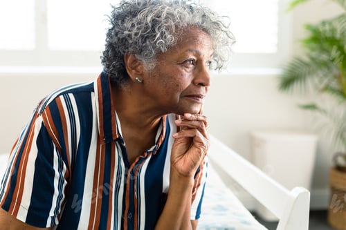 Preview: Portrait of thoughtful african american senior woman sitting on bed and look into distance