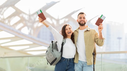 Preview: Cheerful young couple ready for trip, raising boarding passes and passports